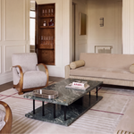 A modern living room interior featuring a beige upholstered sofa with striped detailing, a matching armchair, a dark green marble coffee table, and a large sculptural white pendant light hanging from the ceiling.
