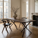 Dining room with wooden table and chairs in a well-lit room with large windows.